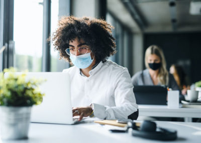 man sat at a laptop wearing a mask to protect against the coronavirus